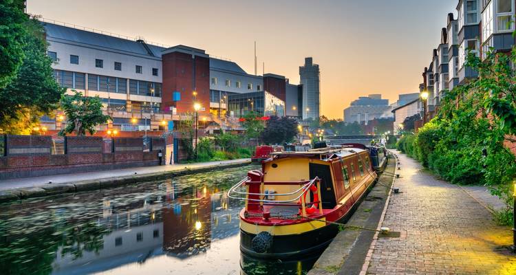 Péniche colorée amarrée le long du canal de Birmingham avec des bâtiments modernes à l'aube.