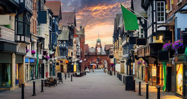 Rue piétonne historique à Chester bordée de bâtiments noir et blanc et l'horloge Eastgate au coucher du soleil.