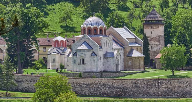 Steinernes orthodoxes Kloster, das von Schutzwällen in einem grasbewachsenen Tal umgeben ist.