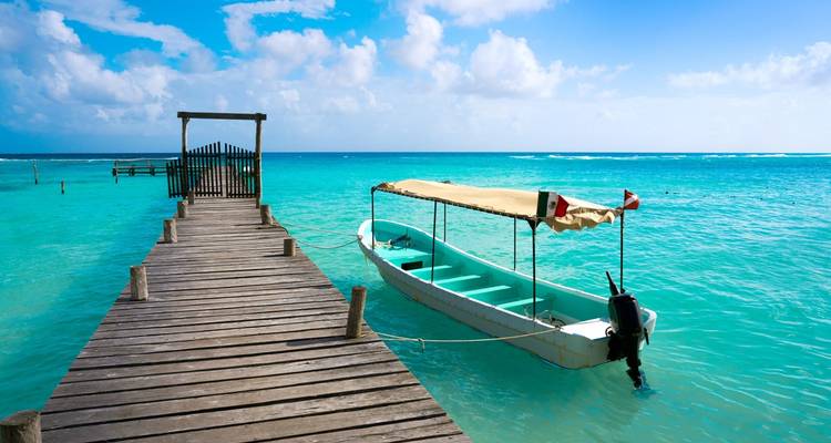 Muelle de madera que lleva a una pequeña barca turquesa en las aguas cristalinas del Caribe bajo cielos soleados.