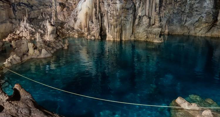 Cenote subterráneo con poca luz, agua azul profundo y formaciones de piedra caliza dramáticas.