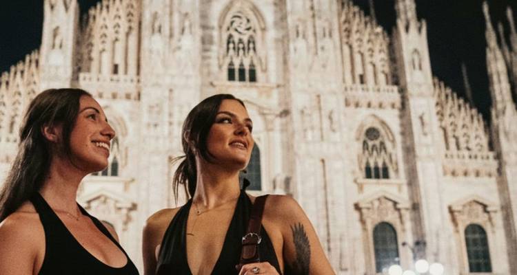 Deux femmes se tiennent dans la lumière du soir devant la Cathédrale de Milan illuminée