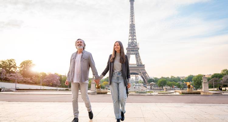 Couple souriant se tenant par la main se promenant près de la Tour Eiffel dans la douce lumière du petit matin.