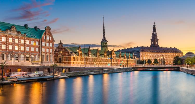 Vue en soirée de la Bourse historique de Copenhague et du Palais de Christiansborg se reflétant dans les eaux calmes du canal au coucher du soleil.