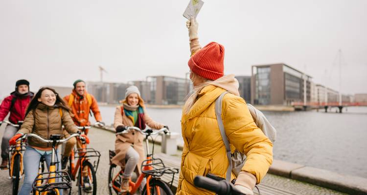 Un groupe de cyclotourisme suit un guide qui lève une carte près du front de mer de Copenhague par un jour couvert.