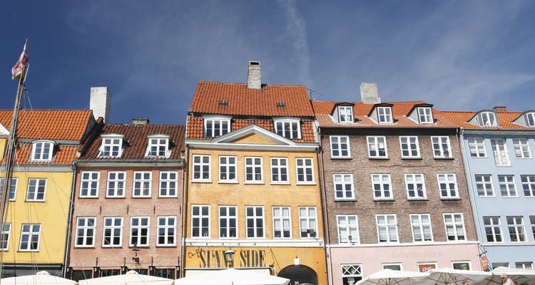 Eine Reihe von pastellfarbenen Kopenhagener Häusern mit orangefarbenen Dächern unter einem tiefblauen Himmel.