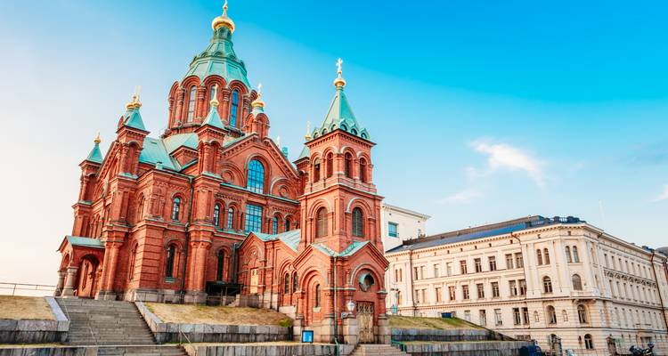 Die rote Backsteinkathedrale Uspenski erhebt sich vor einem klaren blauen Himmel von Helsinki mit benachbartem neoklassizistischem Gebäude.