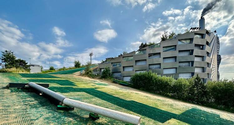 Moderne CopenHill-Müllverbrennungsanlage mit ihrer geneigten künstlichen Skipiste unter einem teilweise bewölkten Himmel.