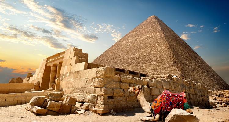 Majestätische Große Pyramide von Giza unter einem leuchtenden Himmel mit einem farbenfroh geschmückten Kamel, das neben antiken Steinblöcken ruht.