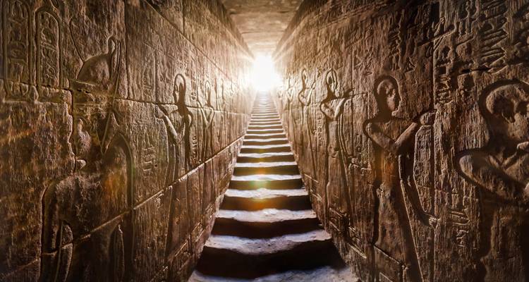 Corridor de pierre gravé de hiéroglyphes menant à un escalier illuminé dans un temple égyptien antique.