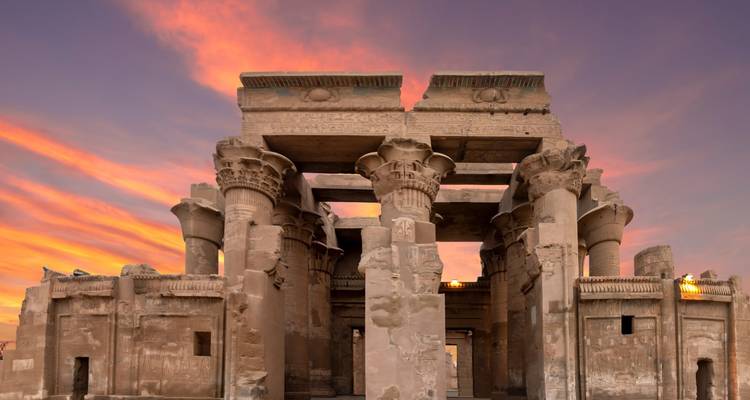 Les colonnes et les murs de grès du temple de Kom Ombo brillant sous un ciel de coucher de soleil dramatique.
