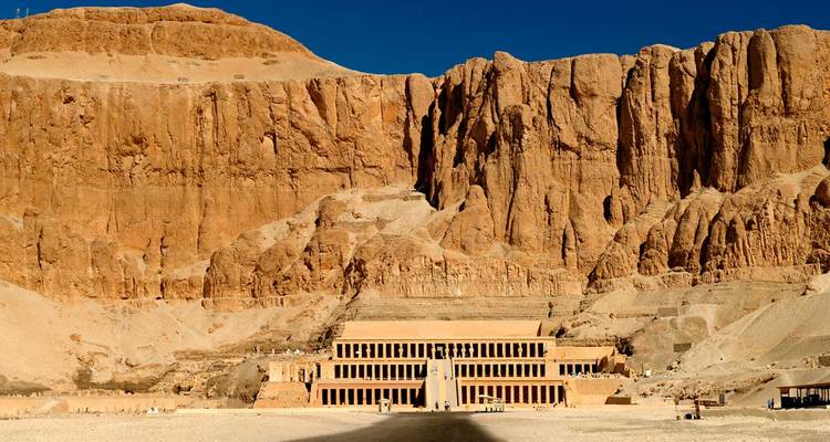 Le Temple d'Hatshepsout niché contre des falaises imposantes dans la Vallée des Rois sous un ciel bleu profond.