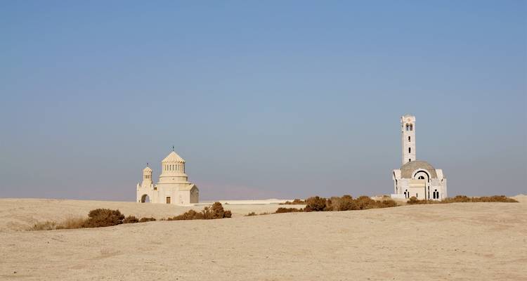 Deux sanctuaires désertiques isolés – l'un ressemblant à une église, l'autre minaret – sur un plateau sablonneux sous un ciel pâle