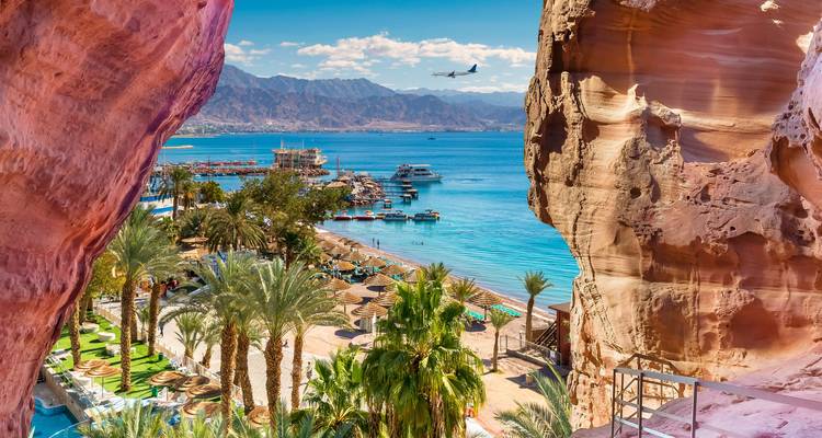 Fenêtre rocheuse encadrant la station balnéaire d'Aqaba et la mer Rouge avec un avion en descente au-dessus