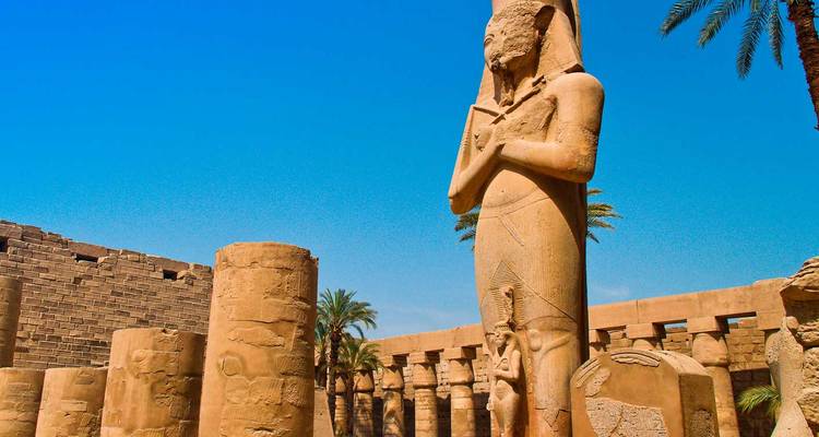 Statue du Pharaon Ramsès II parmi les colonnes gigantesques du Temple de Karnak sous un ciel bleu dégagé