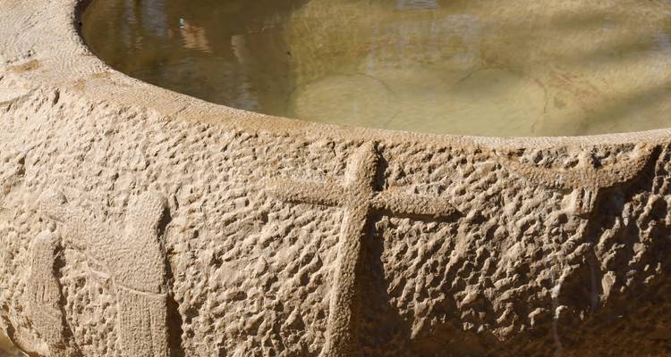 Nahaufnahme eines geschnitzten Steintaufbeckens mit einem Kreuzmotiv, das mit Wasser gefüllt ist