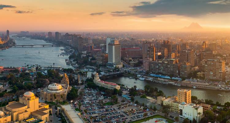 Panoramablick auf den Sonnenuntergang über Kairo mit dem Nil, der sich durch die Stadt schlängelt, und entfernten Pyramiden am Horizont