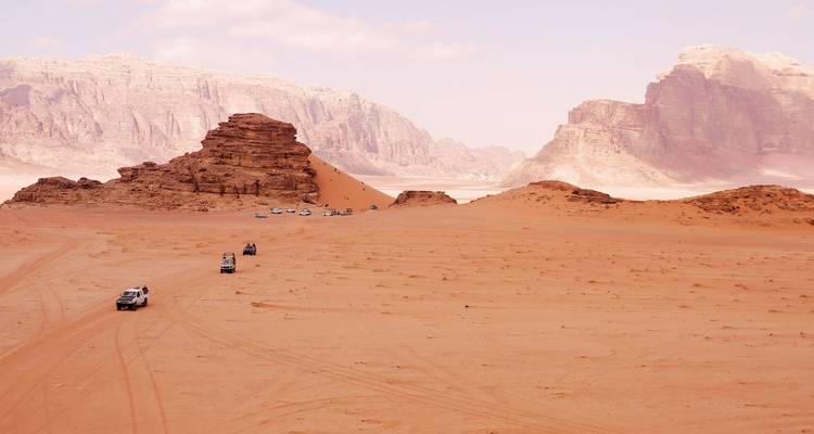 Konvoi von 4x4-Jeeps, die den rosa Sanden des Wadi Rum mit aufragenden Felsformationen durchquert.