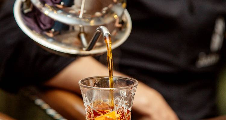 Hete thee stroomt uit de tuit van een ketel in een facetglas met ijs en citrusvruchten.