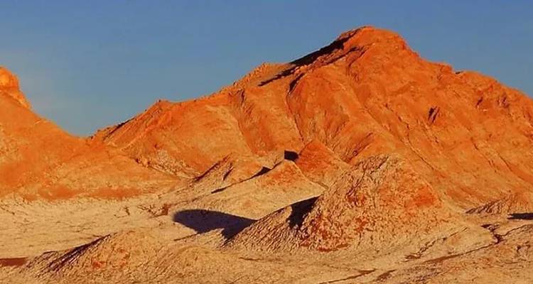 Picos de arenisca rojiza y piso desértico lavado por sal del Valle de la Luna bañados en luz cálida.