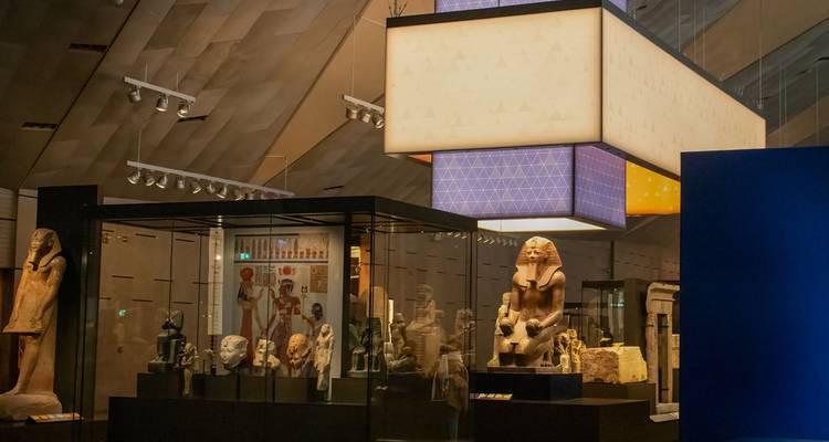 Galerie de musée moderne présentant des statues égyptiennes et des artefacts sous un éclairage élégant.
