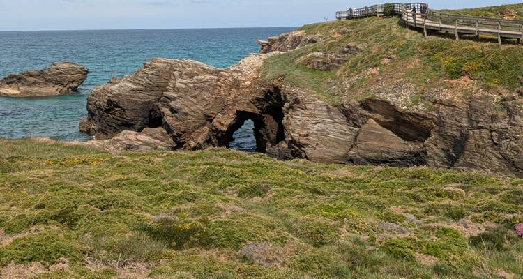 Arche naturelle sculptée dans des falaises côtières escarpées à proximité d'une eau turquoise et d'une promenade