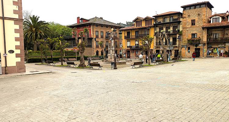 Place pavée ouverte avec des arbres taillés, des bâtiments historiques et de petits groupes de touristes