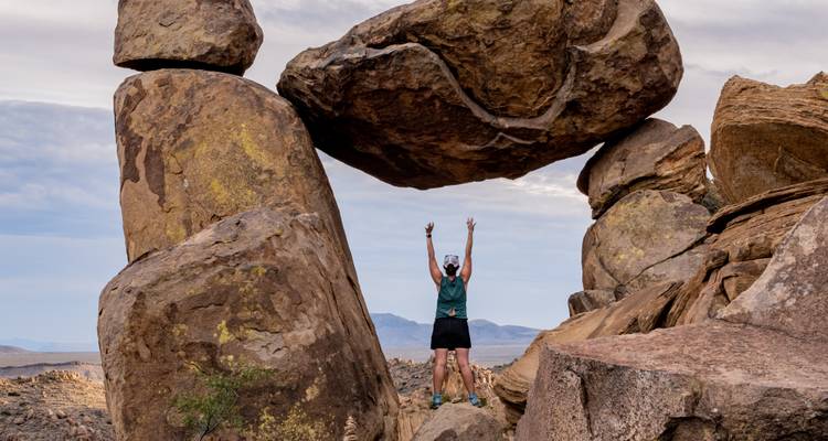 Adventurous hiker cheering beneath a massive balancing rock formation