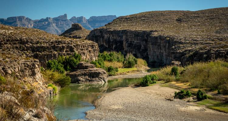 Calm river winding through rugged desert canyon with distant mesas