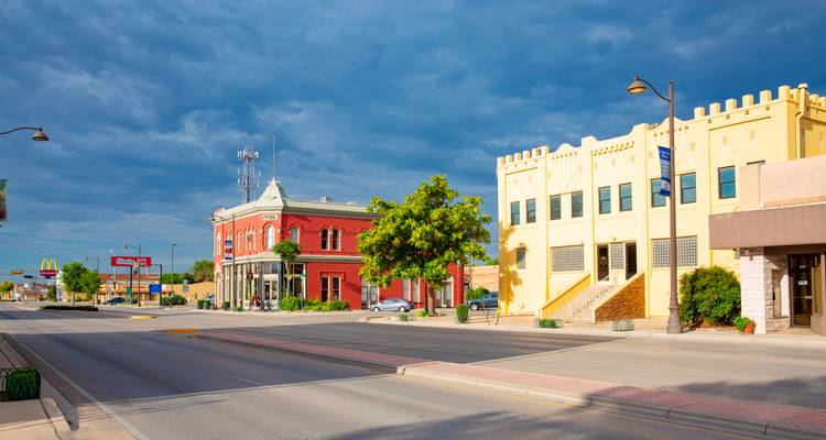 Quiet small-town main street with bright buildings under dramatic clouds