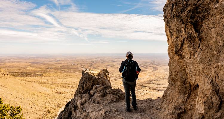 Hiker standing on rocky ledge overlooking vast desert plains