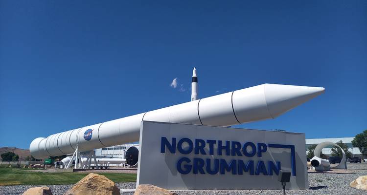 Großer weißer Raketenverstärker mit NASA-Logo und Northrop-Grumman-Schriftzug auf gepflegtem Rasen.