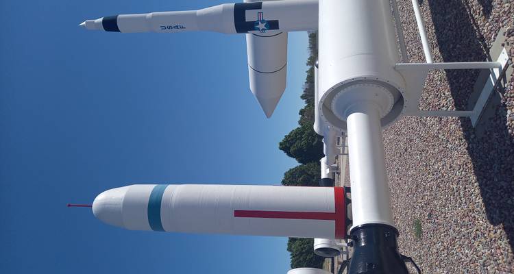 Outdoor-Ausstellung von zwei hohen weißen Raketen vor klarem blauen Himmel in einem Weltraummuseum-Garten.