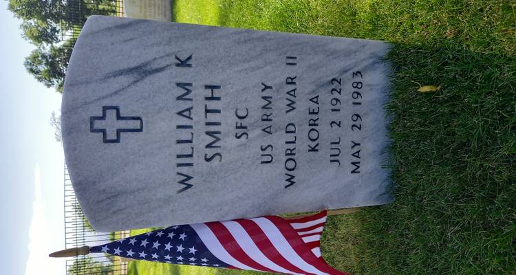 Militärischer Grabstein für William K. Smith mit einer amerikanischen Flagge, die auf grünem Rasen daneben gepflanzt ist.