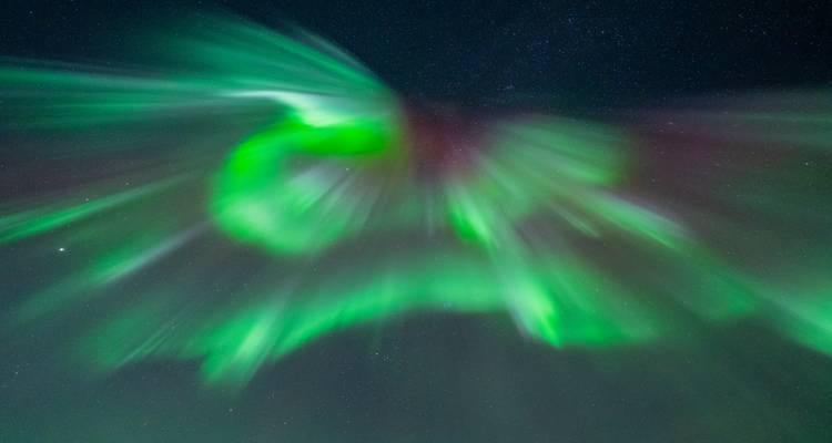 Dynamische uitbarsting van groene aurora stralen die naar buiten uitstralen tegen een sterrenhemels.