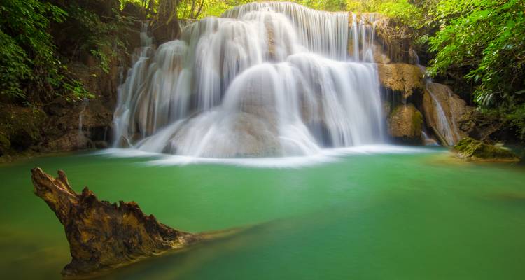 Una cascada de larga exposición sedosa cayendo en cascada hacia una piscina esmeralda en la selva tupida.