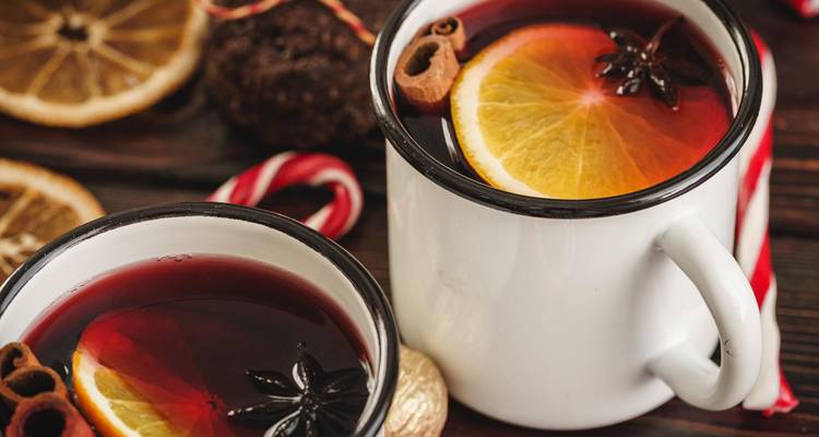 Deux tasses en émail remplies de vin chaud fumant garni de tranches d'orange, d'anis étoilé et de cannelle.