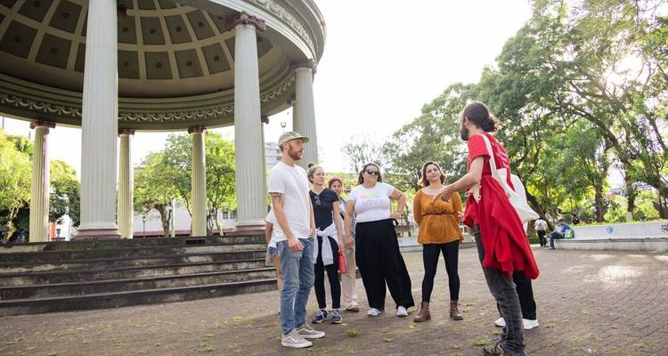 Le guide dirige un petit groupe de touristes à côté d'un belvédère néoclassique dans un parc verdoyant.