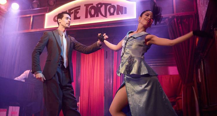 Elegantes bailarines de tango actúan en el escenario del Café Tortoni, bañados por una iluminación dramática.