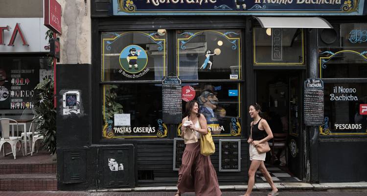 Dos mujeres pasean junto a la fachada de un restaurante vintage en una calle de la ciudad.