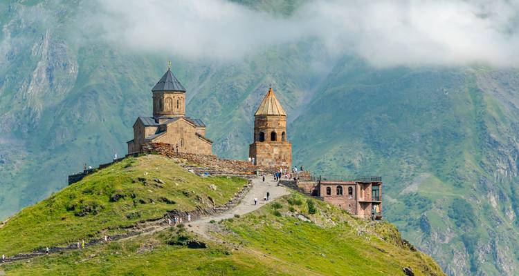 La Iglesia de la Trinidad de Gergeti en lo alto de una colina cubierta de hierba con velos de nubes abrazando los picos del Cáucaso.