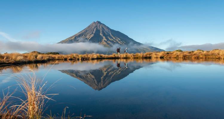 Mont Taranaki se reflétant dans un petit lac alpin immobile avec des randonneurs sur la crête