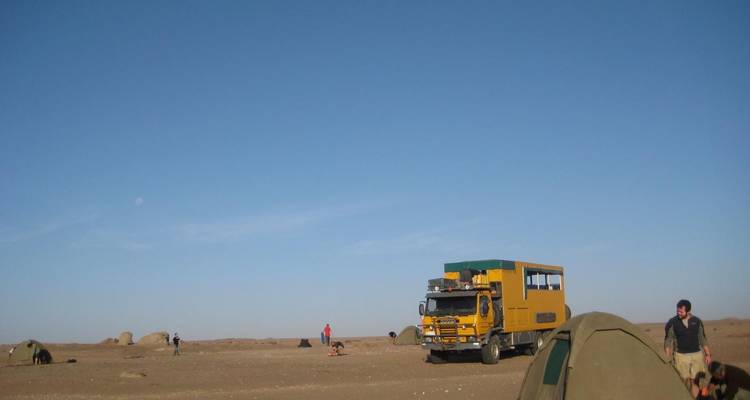 Desert landscape with a yellow truck and tents.