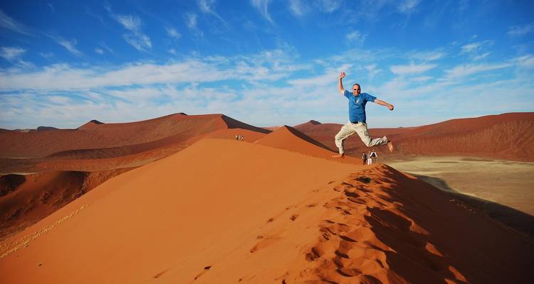 Person jumping on a sand dune with a clear blue sky.