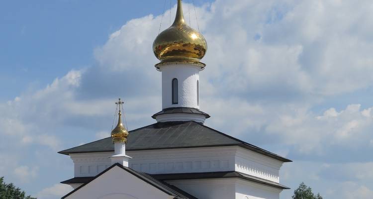 Iglesia ortodoxa blanca con cúpulas de cebolla doradas bajo un cielo parcialmente nublado.