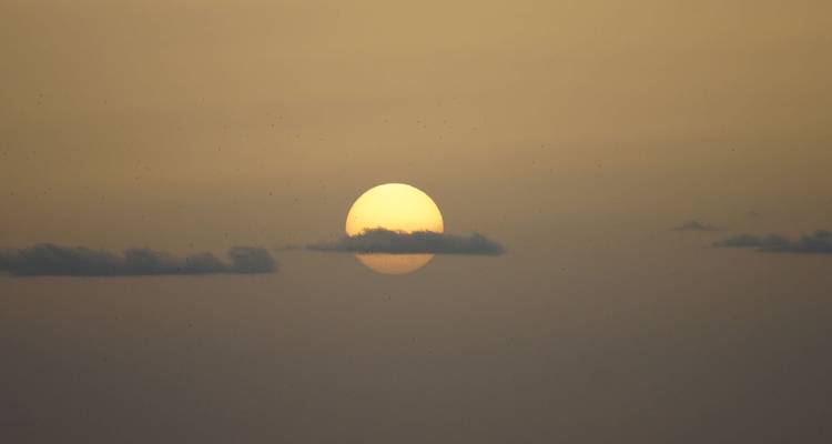 Vista minimalista del sol en el horizonte parcialmente velado por una delgada banda de nubes.