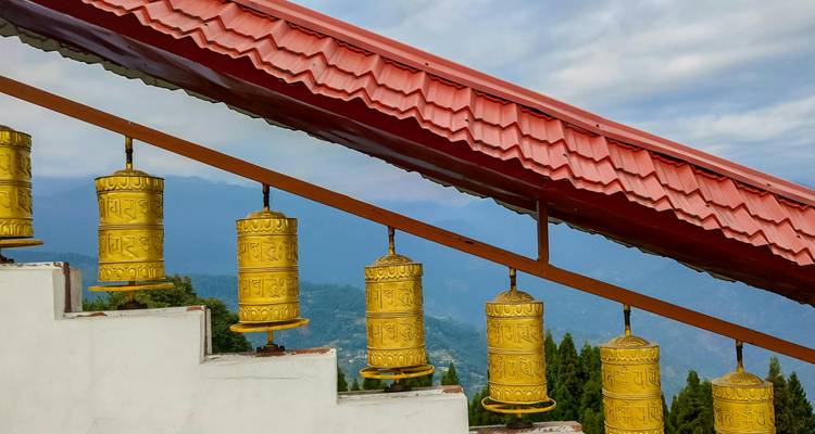 Ruedas de oración budistas doradas en una escalera con crestas del Himalaya brumosas a lo lejos.