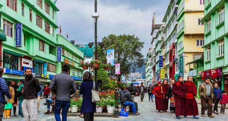 Calle peatonal muy animada llena de edificios coloridos y gente comprando, incluyendo monjes con túnicas rojas.