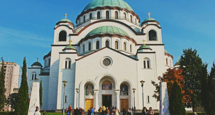 Grande église en marbre blanc avec des dômes verts dominant les visiteurs dans une plaza ensoleillée