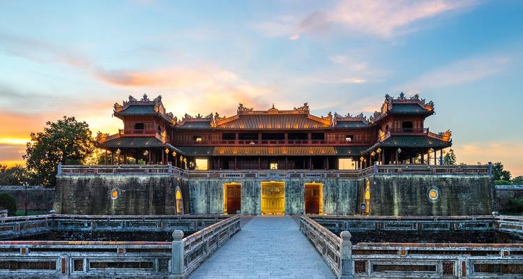 Majestätisches kaiserliches Tor und Palastmauern in der Dämmerung mit lebendigem Sonnenuntergangshimmel und steinerner Brücke, die zum Eingang führt.